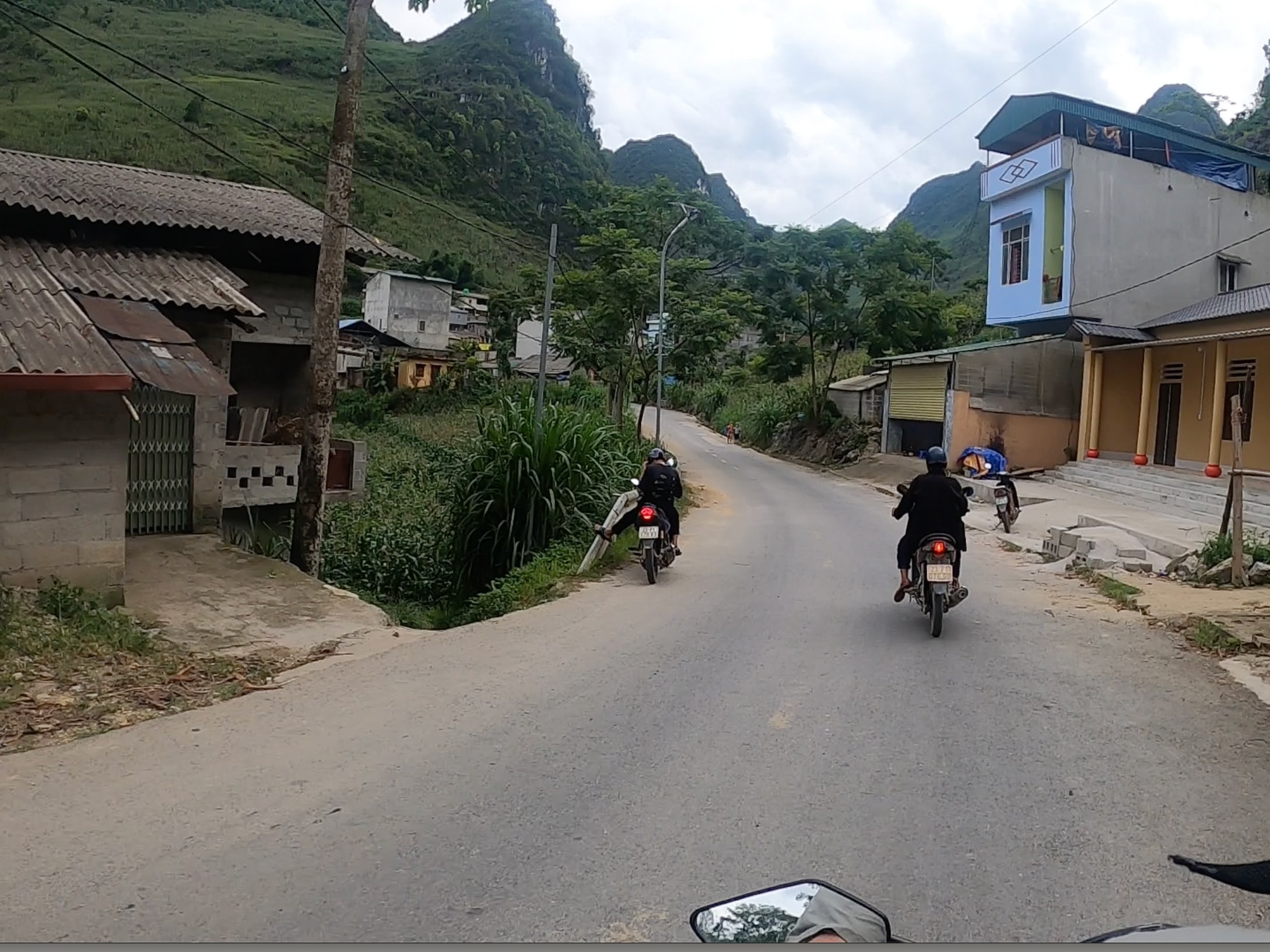 Motorcycles travel along a narrow road through a mountain village.